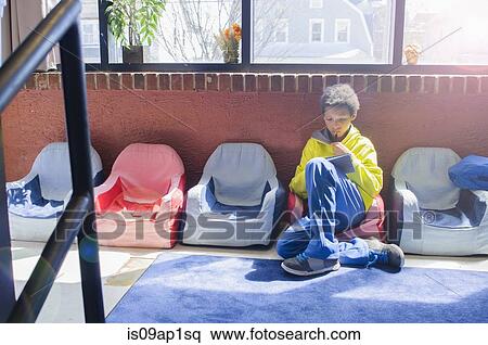 Stock Photography - Boy sitting alone in classroom using digital tablet. Fotosearch