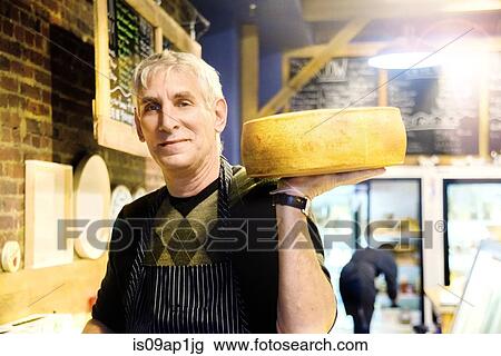 Stock Image - Cheesemonger holding wheel of cheese. Fotosearch