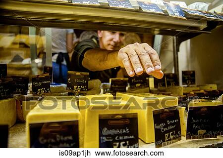 Stock Image - Cheesemonger reaching for cheese in display. Fotosearch