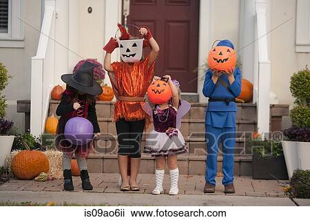 Stock Image - Children covering face with Jack O' Lantern bucket in front of house. Fotosearch