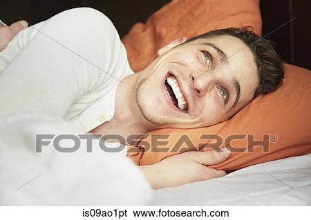 Close up of young man lying in bed and laughing View Large Photo Image Stock Photograph - Close up of young man lying in bed and laughing. Fotosearch