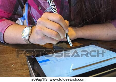 Stock Image - Cropped close up of young woman using pen to touchscreen digital tablet. Fotosearch