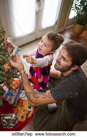 Stock Photography - Father and daughter placing Christmas ornaments on tree. Fotosearch