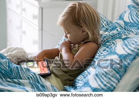 Stock Photo - Female toddler sitting up in bed using digital tablet. Fotosearch