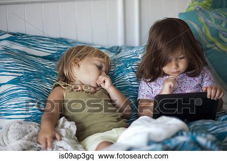Girl and toddler sister reclining in bed using digital tablet View Large Photo Image Stock Photography - Girl and toddler sister reclining in bed using digital tablet. Fotosearch