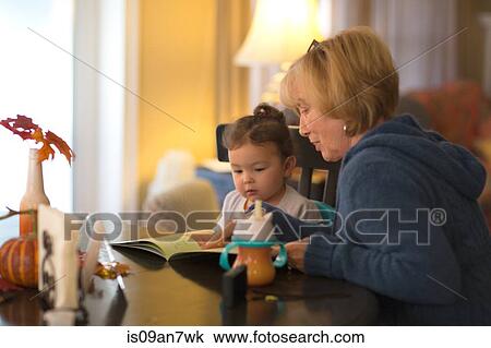 Stock Image - Grandmother and granddaughter reading together at home. Fotosearch