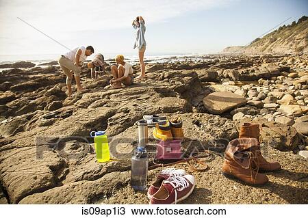 Stock Image - "Group of friends exploring rock pools on beach, shoes and belongings in foreground". Fotosearch