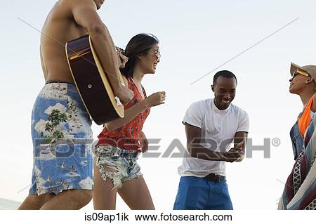 Stock Image - Group of friends singing and playing guitar on beach. Fotosearch