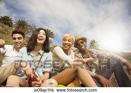Stock Image - "Group of friends sitting on hill, laughing". Fotosearch