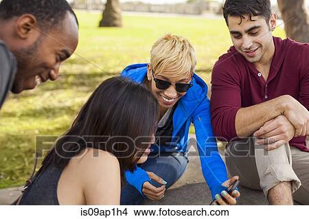 Picture - "Group of friends sitting together, woman showing screen of smartphone". Fotosearch