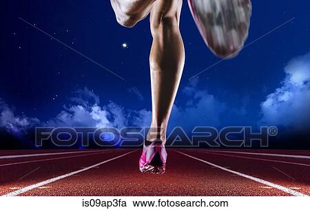 Stock Image - Legs of young female athlete running on race track at night. Fotosearch