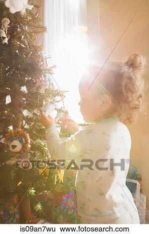 Stock Photograph - Little girl admiring Christmas ornaments on tree. Fotosearch