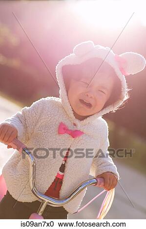 Stock Image - Little girl learning to ride tricycle. Fotosearch