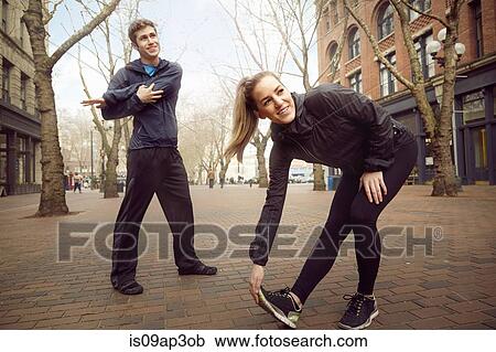 Stock Image - "Male and female runners warming up on tree lined street, Pioneer Square, Seattle, USA". Fotosearch