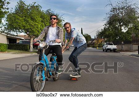 Male skateboarder skitching on friends moped on suburban road View Large Photo Image Stock Photo - Male skateboarder skitching on friends moped on suburban road. Fotosearch