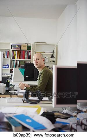 Stock Image - "Mature man at desk in creative studio, portrait". Fotosearch