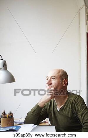 Stock Photo - Mature man at desk with hand on chin. Fotosearch