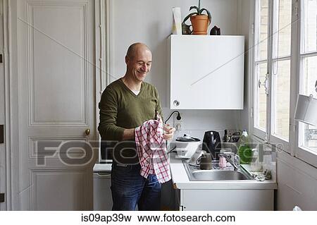 Mature man drying glass at kitchen sink View Large Photo Image Stock Photo - Mature man drying glass at kitchen sink. Fotosearch