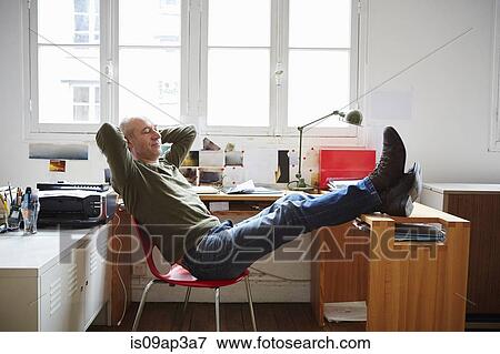 Stock Photo - Mature man sitting with feet up at desk. Fotosearch
