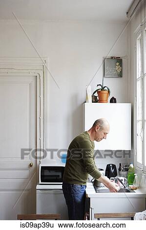 Stock Photograph - Mature man washing up in kitchen. Fotosearch
