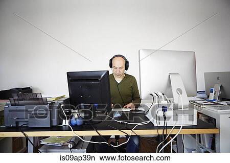 Picture - Mature man working in creative studio wearing headphones. Fotosearch