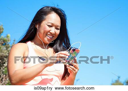 Stock Photo - "Mid adult woman in sports clothing, wearing earphones, holding smartphone". Fotosearch