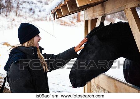 Picture - Mid adult woman petting horse in stable. Fotosearch