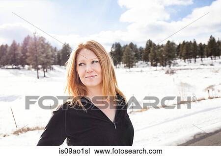 Stock Image - Mid adult woman standing on snowy roadside. Fotosearch