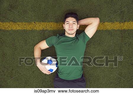 Overhead portrait of young male soccer player lying on football pitch View Large Photo Image Stock Photo - Overhead portrait of young male soccer player lying on football pitch. Fotosearch