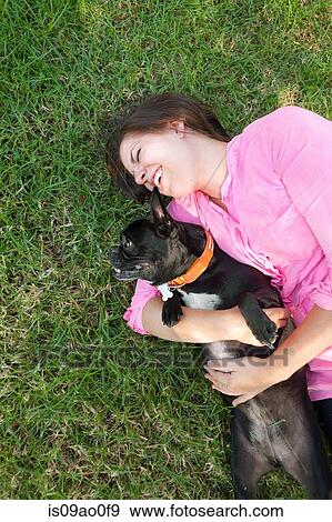Stock Photo - Overhead view of young woman lying in park playing with dog. Fotosearch