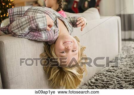 Stock Image - Portrait of boy lying upside down over sofa at christmas. Fotosearch