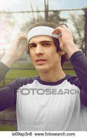 Stock Photograph - Portrait of mid adult male soccer player adjusting headband on soccer pitch. Fotosearch