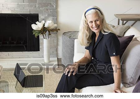 Stock Photograph - "Portrait of senior female businesswoman sitting on sofa, smiling". Fotosearch