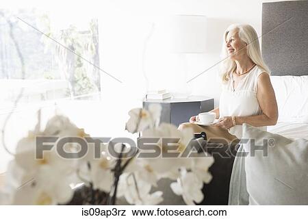 Portrait of senior woman sitting on bed with cup of tea View Large Photo Image Stock Photo - Portrait of senior woman sitting on bed with cup of tea. Fotosearch