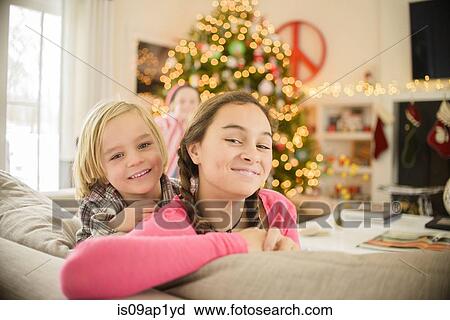 Stock Image - Portrait of teenage girl and brother leaning on sofa at christmas. Fotosearch