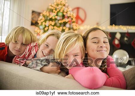 Stock Image - Portrait of teenage girl and brothers on sofa at christmas. Fotosearch