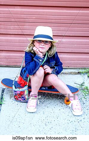 "Portrait of young girl wearing tutu, denim jacket and hat, sitting on skateboard" View Large Photo Image Picture - "Portrait of young girl wearing tutu, denim jacket and hat, sitting on skateboard". Fotosearch