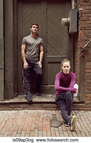 Stock Image - Portrait of young male and female runners in alleyway. Fotosearch