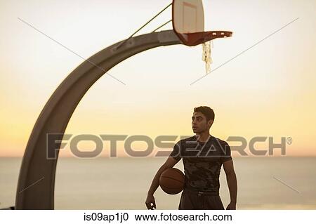 Stock Image - "Portrait of young man holding basketball, outdoors". Fotosearch
