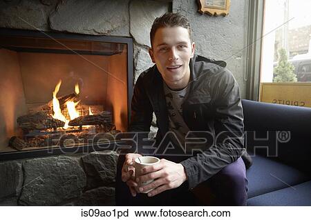 Stock Image - Portrait of young man sitting by open fire in cafe. Fotosearch