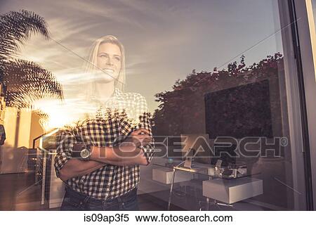 Stock Photography - Portrait of young woman watching sunset from suburban window. Fotosearch