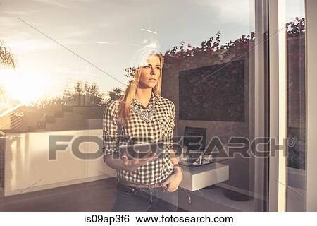 Portrait of young woman with digital tablet gazing from suburban window View Large Photo Image Stock Photograph - Portrait of young woman with digital tablet gazing from suburban window. Fotosearch