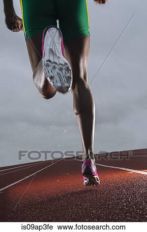Stock Image - Rear view of young female athletes legs running on race track. Fotosearch