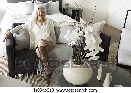 Senior woman sitting on sofa in stylish bedroom View Large Photo Image Stock Photo - Senior woman sitting on sofa in stylish bedroom. Fotosearch
