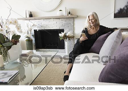 "Senior woman sitting on sofa, looking at her phone" View Large Photo Image Stock Image - "Senior woman sitting on sofa, looking at her phone". Fotosearch