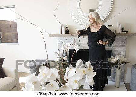 Stock Image - "Senior woman standing in stylish living room, looking at her phone". Fotosearch