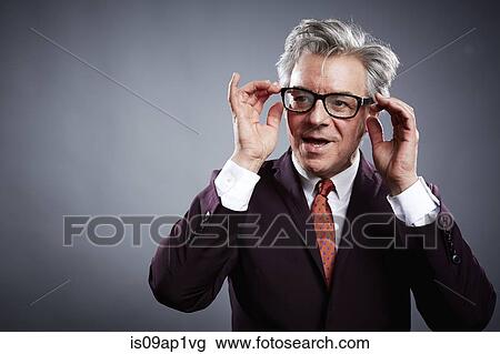 Stock Image - Studio portrait of mature businessman adjusting his spectacles. Fotosearch