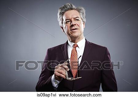 Stock Image - Studio portrait of mature businessman holding his spectacles. Fotosearch