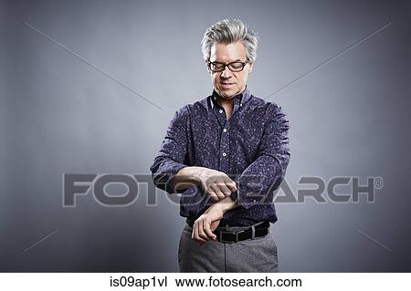 Stock Image - Studio portrait of mature businessman rolling up his sleeves. Fotosearch