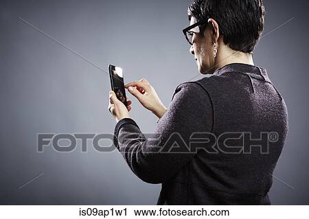 Stock Image - Studio portrait of mature businesswoman using touchscreen on smartphone. Fotosearch